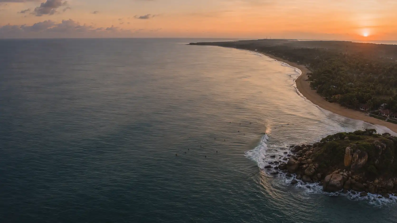 Aerial view of Arugam Bay at dawn with the point break, the curving beach and palm-covered coast